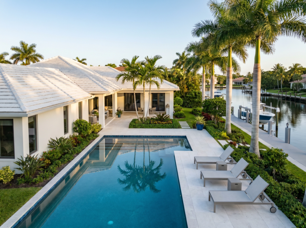 A luxury waterfront estate in Jupiter featuring a white flat tile roof, modern pool deck, and a private boat dock on a canal.