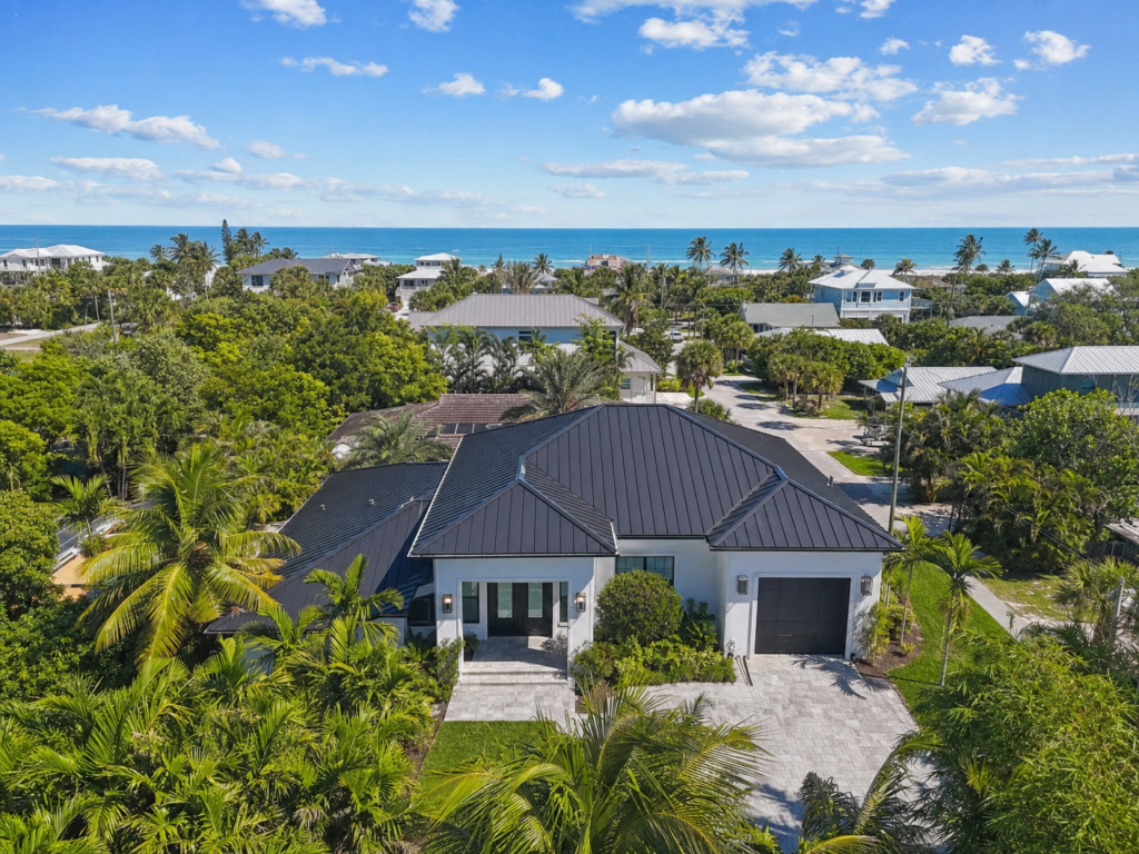 A modern coastal home in North Palm Beach featuring a dark charcoal standing seam metal roof and tropical landscaping.