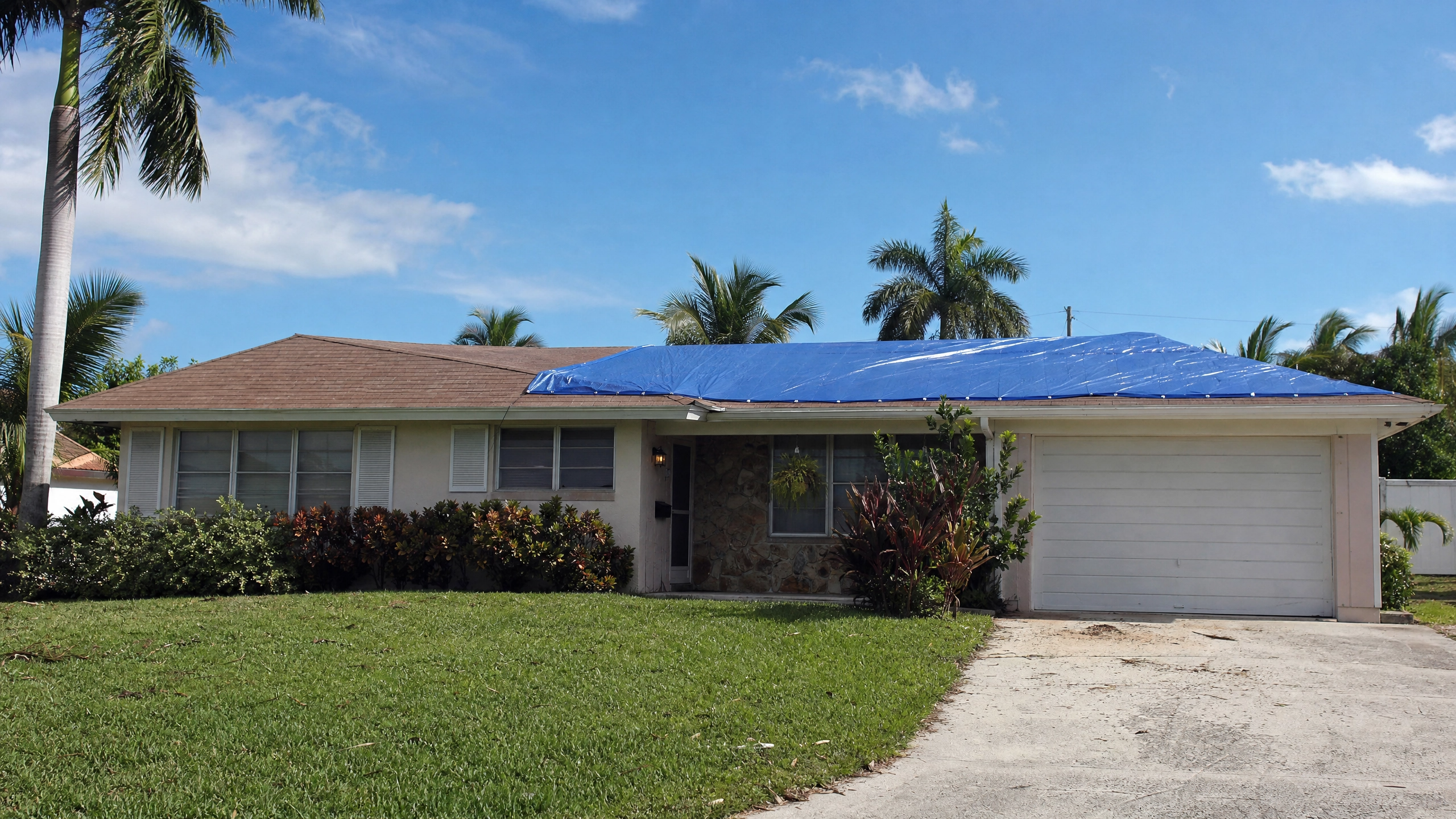 A professional roof tarping job on a typical 1970s-80s ranch-style home in Riviera Beach, Florida, after storm damage.