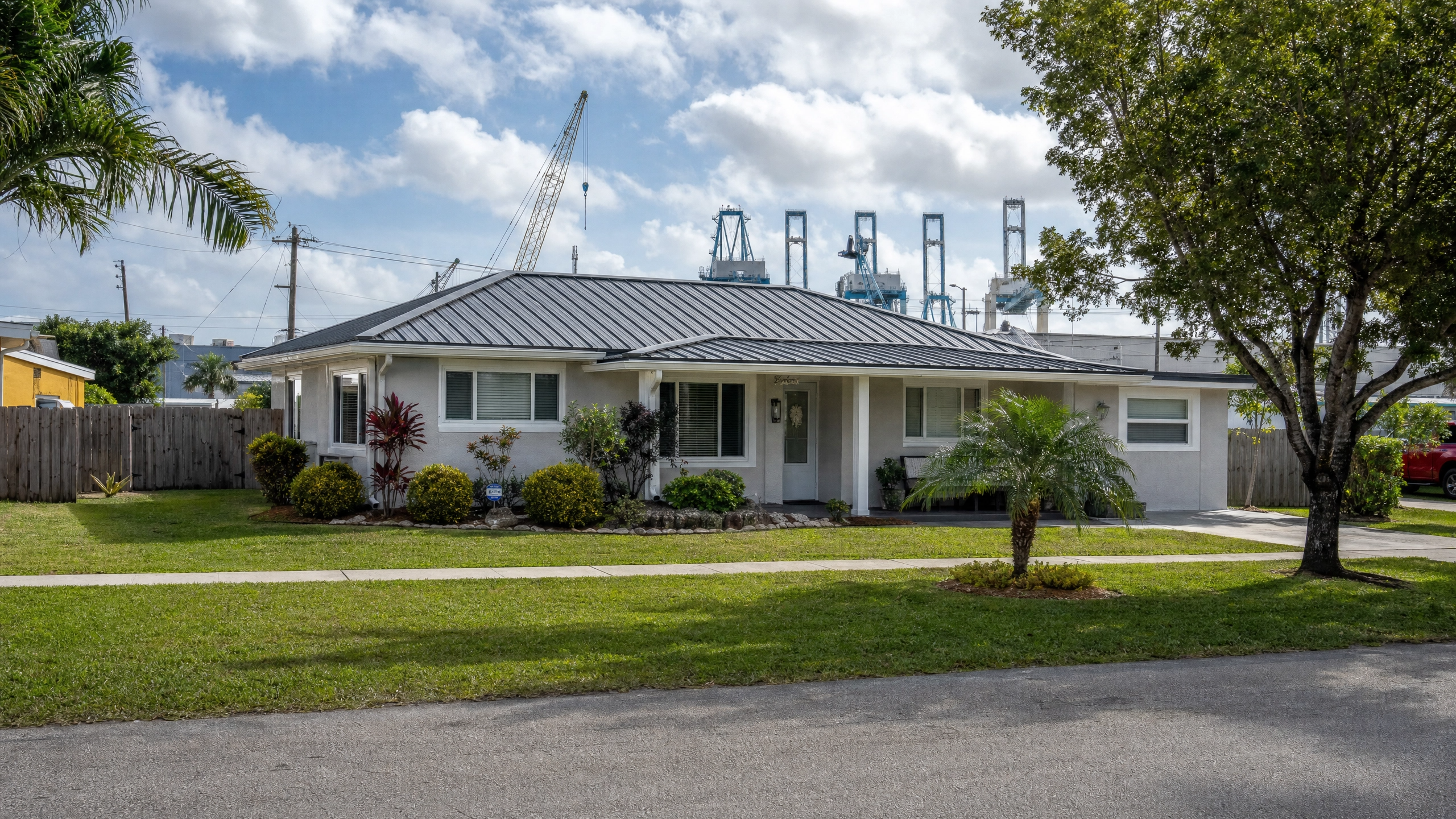 A well-maintained single-story home in Riviera Beach with a durable metal roof, with the Port of Palm Beach cranes visible in the background.